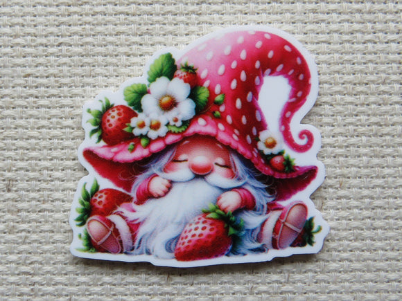 First view of an adorable sitting red gnome with a strawberry hat minder. The gnome is holding a strawberry and the hat has a small strawberry with white strawberry blossoms.