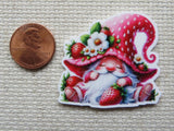 Second view of an adorable sitting red gnome with a strawberry hat minder. The gnome is holding a strawberry and the hat has a small strawberry with white strawberry blossoms.