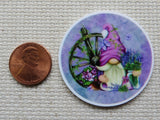 Second view of Pinkish purple gnome in a purple circle with a wagon wheel and a vase of lavender flowers minder.