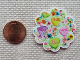 Second view of Four hearts nestled in a background of flowers minder. The green heart says "Be Mine". The yellow heart says "Kiss". The pink heart says "Love". The purple heart says "XOXO".