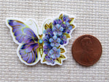 Butterfly-shaped minder with floral design next to a penny.