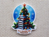 Small Christmas tree sitting on top of a stack of colorful books with a string of lights in front of a winter night circle with the words "All booked for Christmas" minder.