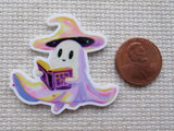 Cartoon ghost with a witch hat reading a book minder, next to a penny for scale, on a textured surface.