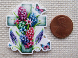Decorative cross with flowers and butterflies next to a penny.
