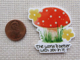 Minder of a red mushroom with white spots and yellow flowers, featuring the text 'The world is better with you in it', next to a penny for scale.