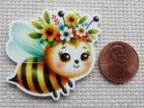 Minder of a bee with floral headband next to a penny.