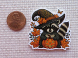 Halloween-themed minder of a raccoon in a witch hat with a pumpkin, next to a penny for scale.