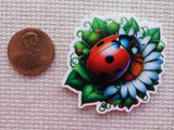 Colorful ladybug and flower minder next to a penny on a textured surface