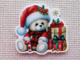 Minder of a teddy bear in a Santa hat with Christmas presents on a textured beige background.