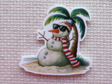 Minder of a snowman with sunglasses and a scarf standing next to a palm tree on a textured surface.