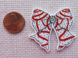 Decorative bow minder with red and white pattern next to a penny on a textured surface