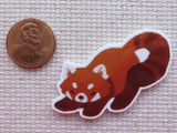 Minder of a red panda next to a penny on a textured surface