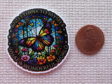 Minder with butterfly design and text next to a penny on a textured surface