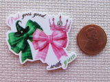 Minder with green and pink bows and a crown, next to a penny for scale.