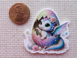 Colorful minder of a baby dragon with butterfly wings next to a penny on a textured surface
