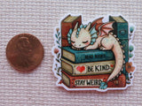 Minder of a dragon lying on books with motivational phrases, next to a penny for scale.