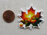 Colorful leaf-shaped minder with a pumpkin design next to a penny on a textured surface