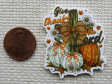 Decorative minder with pumpkins, flowers, and text 'Give thanks to the Lord' next to a penny for scale.