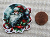 Decorative minder of Santa Claus with holly leaves and berries next to a penny for scale.