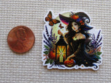 Minder of a witch with a lantern and pumpkins next to a penny for scale on a textured surface.