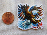 Minder of an eagle with an American flag design next to a penny on a textured surface