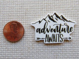Minder with 'adventure awaits' text next to a penny on a textured surface