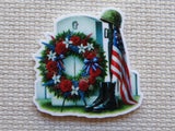 First view of a Simple military grave stone minder with a patriotic wreath hanging in front of it. A flag is next to it with military boots at the bottom and a helmet on the top of the flagpole.