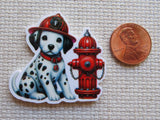 Minder of a dalmatian puppy in a fire helmet next to a red fire hydrant, with a penny for scale on a textured beige background.