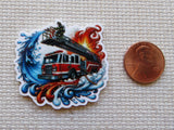 Minder of a fire truck with flames and water next to a penny for scale on a textured surface.