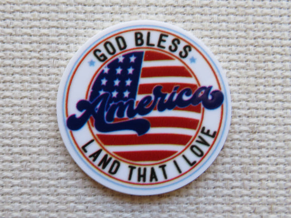 Round minder with 'God Bless America Land That I Love' text and American flag design on a textured beige background.