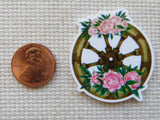 Decorative wheel minder with pink flowers next to a penny on a textured surface