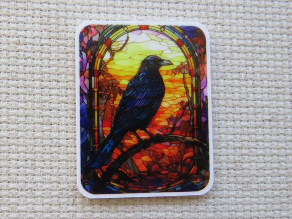Minder with a colorful design of a bird on a branch against a stained glass-like background, placed on a textured surface.