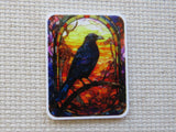 Minder with a colorful design of a bird on a branch against a stained glass-like background, placed on a textured surface.