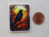 Minder with a colorful bird design next to a penny on a textured surface