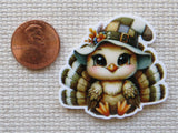 Minder of a cute turkey wearing a pilgrim hat next to a penny for scale on a textured surface.