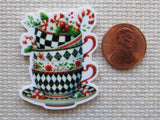 Decorative teacup minder with holiday elements next to a penny on a textured surface