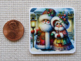 Decorative minder of Santa Claus and a girl with a penny for scale on a textured surface.