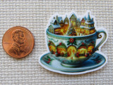 Minder of a teacup with a Christmas village design next to a penny for scale.