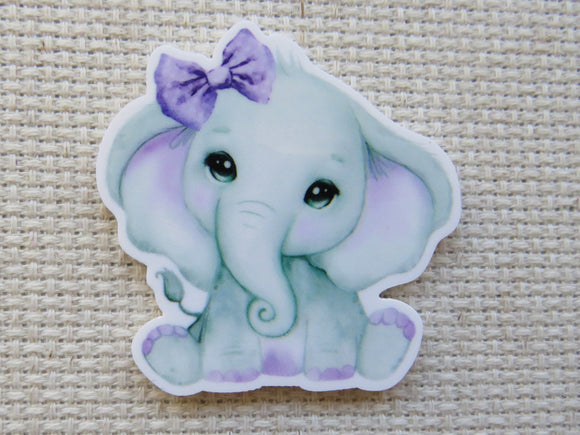 Minder of a cute elephant with a purple bow on a textured beige background
