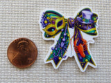 Colorful Mardi Gras-themed minder with a mask and top hat next to a penny for scale on a textured surface.