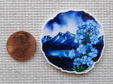 Minder with blue floral design and mountain landscape next to a penny on a textured surface