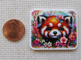 Colorful minder of a red panda surrounded by flowers next to a penny for scale on a textured surface.