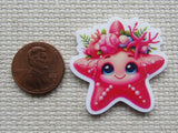 Minder of a pink starfish with floral crown next to a penny on a textured surface