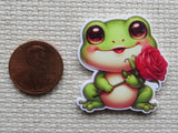 Minder of a cartoon frog holding a rose next to a penny on a textured surface