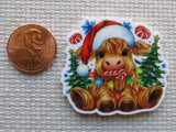 Minder of a cow in a Santa hat with Christmas decorations next to a penny on a textured surface