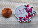 Minder with butterflies and 'Life is Beautiful' text next to a penny on a textured surface
