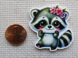 Minder of a raccoon with flowers next to a penny on a textured surface