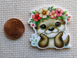 Minder of a cute otter with a floral headband next to a penny on a textured surface