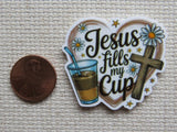 Minder with 'Jesus fills my cup' text and a cross, next to a penny for scale, on a textured beige background.
