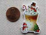 Christmas-themed minder of a iced coffee with snowmen and a tree next to a penny for scale.